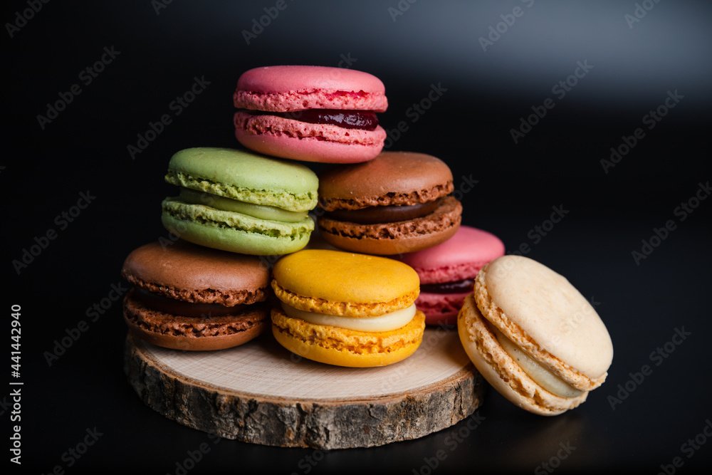 Macarons cookie dessert from France in a stack on wooden board and black background Macarons cookie dessert from France in a stack on wooden board and black background