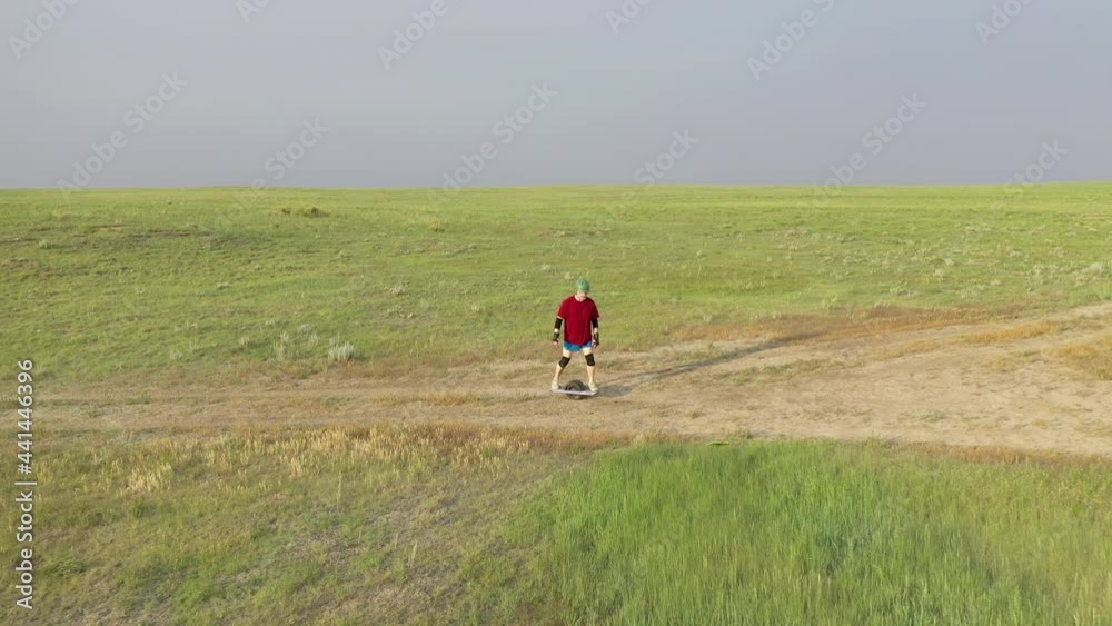 Senior, athletic, overweight male is riding an one-wheeled electric skateboard on a trail in green prairie, Pawnee National Grassland in Colorado, aerial view in early summer Senior, athletic, overweight male is riding an one-wheeled electric skateboard on a trail in green prairie, Pawnee National Grassland in Colorado, aerial view in early summer