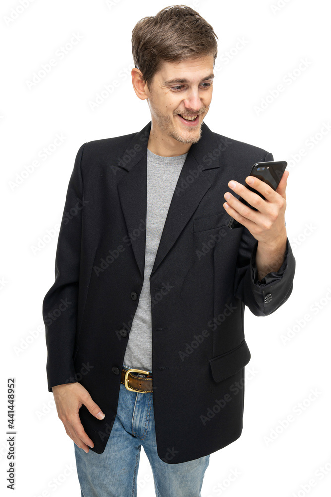 Young handsome tall slim white man with brown hair smiling to his mobile phone in black blazer in blue jeans isolated on white background Young handsome tall slim white man with brown hair smiling to his mobile phone in black blazer in blue jeans isolated on white background