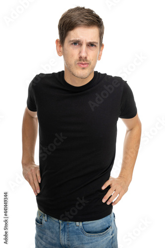 Young handsome tall slim white man with brown hair looking judgingly in black shirt in blue jeans isolated on white background