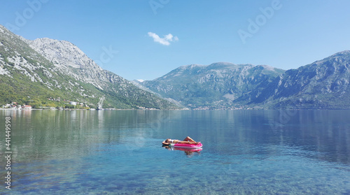 AERIAL. Young women enjoy floating on a mattress at the sea. Mountains on background.