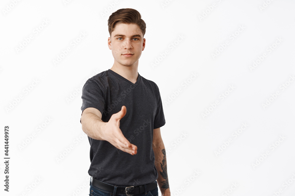 Confident young man stretching hand for handshake, nice to meet you gesture, greeting someone, going on interview, smiling friendly, standing over white background Confident young man stretching hand for handshake, nice to meet you gesture, greeting someone, going on interview, smiling friendly, standing over white background