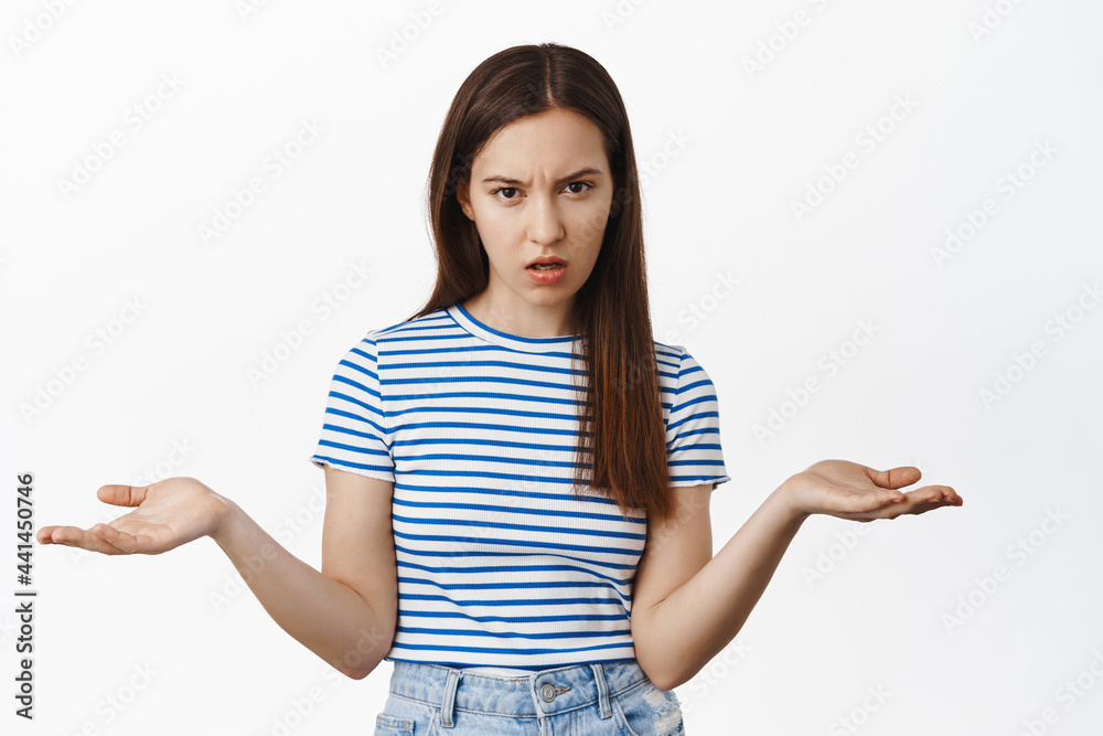So what. Annoyed confused woman stare upset at camera, spread hands sideways and shrugging shoulders, dont understand why, standing against white background So what. Annoyed confused woman stare upset at camera, spread hands sideways and shrugging shoulders, dont understand why, standing against white background