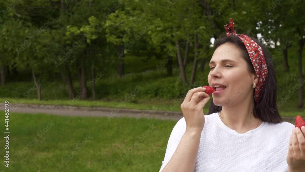 Woman eating red berry strawberry, smiling happy, looking at camera in white t-short. Portrait of mom, wife, farmer, pin up on nature, outdoor Woman eating red berry strawberry, smiling happy, looking at camera in white t-short. Portrait of mom, wife, farmer, pin up on nature, outdoor