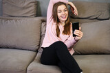 Photo of a young caucasian girl talking on the phone on the sofa while sitting posing with a smile.