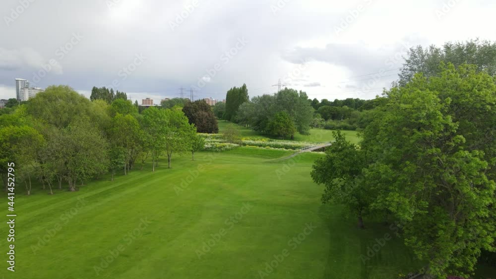 Panorama curve of golf course divided by brook with blooming vegetation on banks. Cityscape in background Panorama curve of golf course divided by brook with blooming vegetation on banks. Cityscape in background