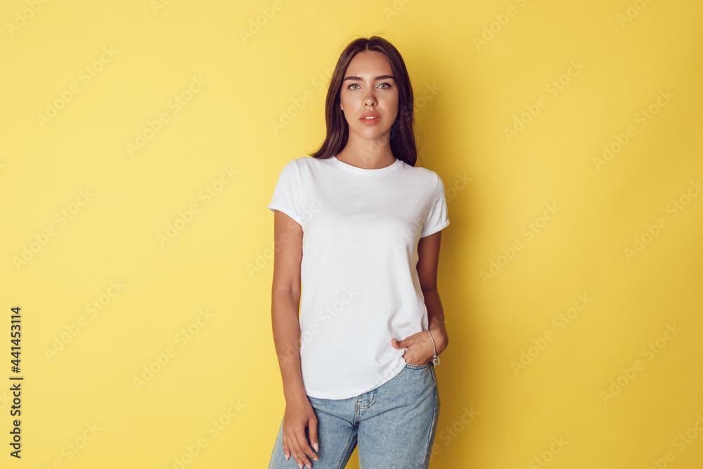 Attractive young woman in a white t-shirt stands on a bright yellow background. Attractive young woman in a white t-shirt stands on a bright yellow background.