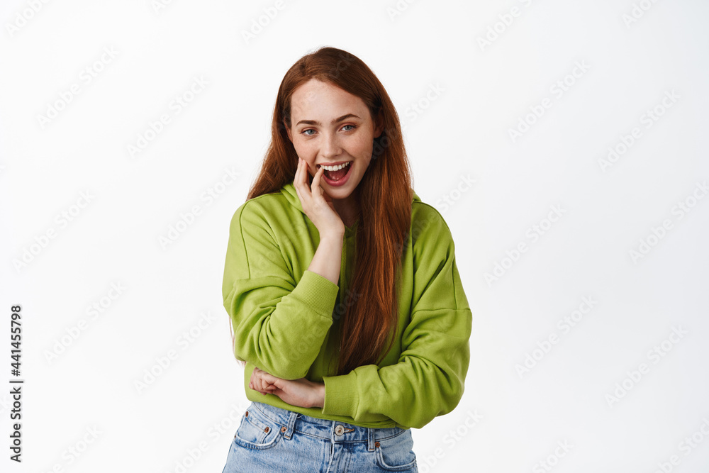 Stylish redhead woman laughing, smiling and looking amused at camera, standing happy in hoodie against white background Stylish redhead woman laughing, smiling and looking amused at camera, standing happy in hoodie against white background
