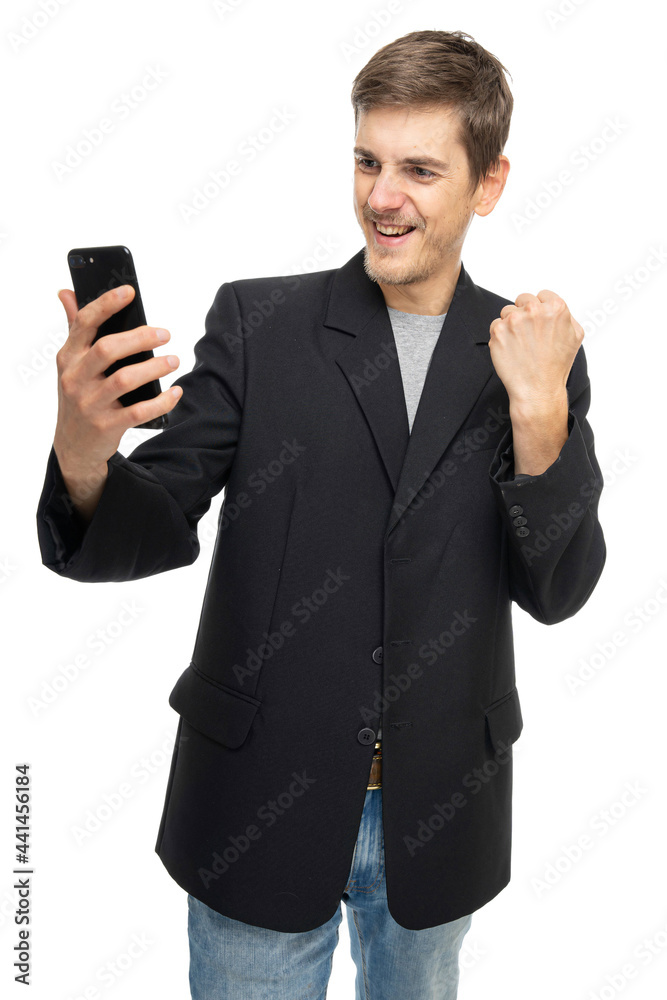 Young handsome tall slim white man with brown hair is thrilled looking to his mobile phone in black blazer isolated on white background Young handsome tall slim white man with brown hair is thrilled looking to his mobile phone in black blazer isolated on white background