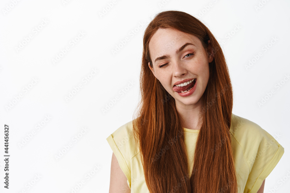 Lifestyle and women. Close up of redhead girl winking and showing tongue, stay positive, looking happy and upbeat, standing in t-shirt over white background Lifestyle and women. Close up of redhead girl winking and showing tongue, stay positive, looking happy and upbeat, standing in t-shirt over white background