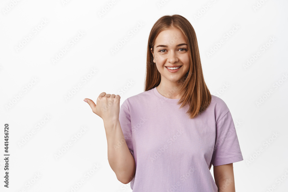 That way. Smiling young woman, girl assistant pointing thumb left and look friendly, showing direction, logo banner on empty space aside, white background That way. Smiling young woman, girl assistant pointing thumb left and look friendly, showing direction, logo banner on empty space aside, white background
