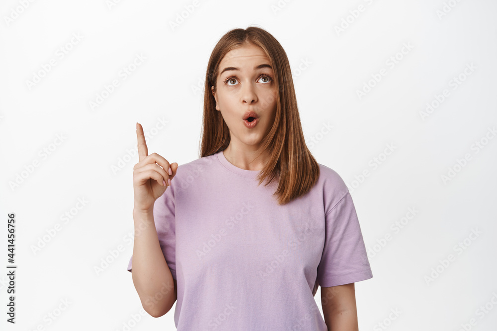 Wow so awesome. Young woman pointing and looking up with fascinated, impressed face, found smth in store worth attention, standing over white background in summer t-shirt Wow so awesome. Young woman pointing and looking up with fascinated, impressed face, found smth in store worth attention, standing over white background in summer t-shirt