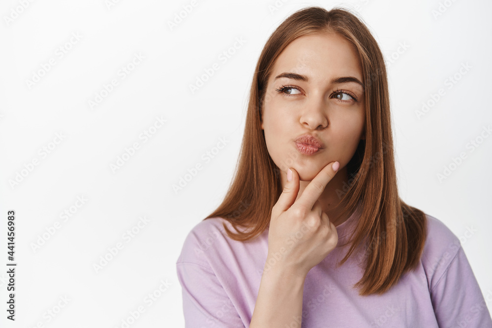 Hmm let me think. Thoughtful young woman rub chin and look away while thinking, ponder decision, makes choice, stands in summer t-shirt against white background