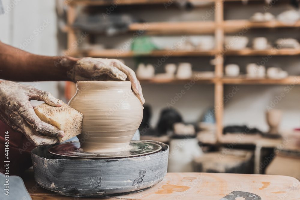 close up view of young african american man holding sponge and making wet clay pot on wheel in pottery - obrazy, fototapety, plakaty 