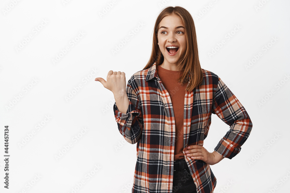 Cheerful female model, pointing and looking left at discount banner, showing smth cool aside, checking out new advertisement, standing against white background Cheerful female model, pointing and looking left at discount banner, showing smth cool aside, checking out new advertisement, standing against white background