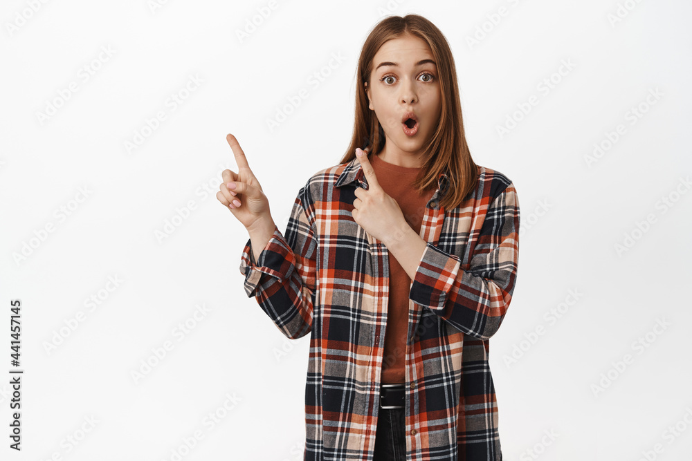 Surprised caucasian woman gasp in awe, pointing at upper left corner with impressed face expression, showing discount promo text, advertisement, white background Surprised caucasian woman gasp in awe, pointing at upper left corner with impressed face expression, showing discount promo text, advertisement, white background