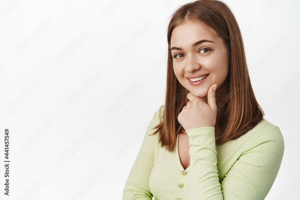 Close up portrait of young confident girl look intrigued, interested in smth, touch chin and smile thoughtful, looking at camera pondering, standing against white background Close up portrait of young confident girl look intrigued, interested in smth, touch chin and smile thoughtful, looking at camera pondering, standing against white background