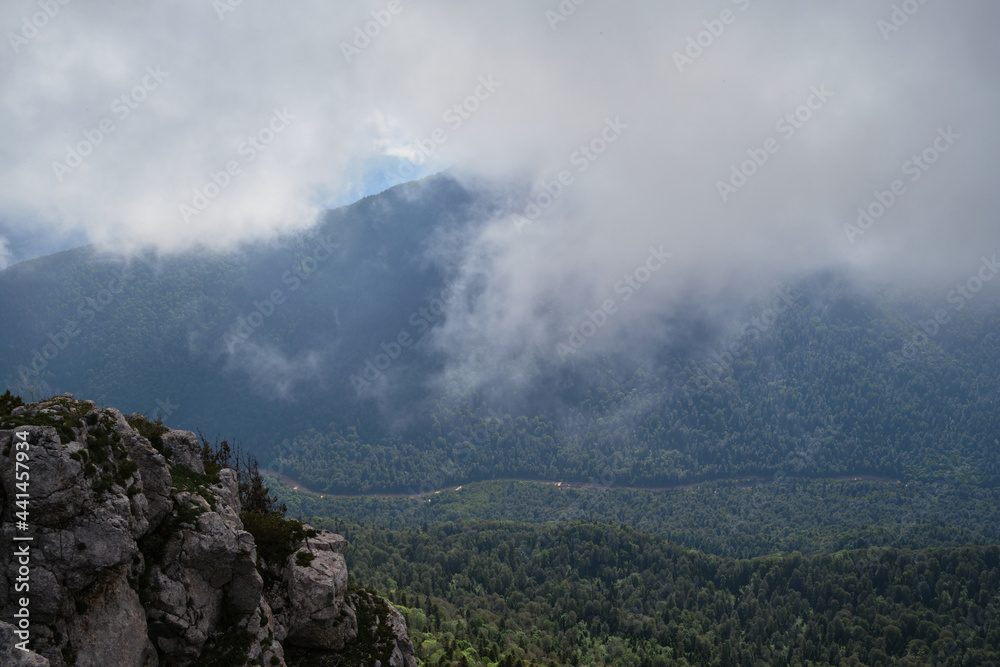 Nature and landscape of national Park in Caucasus. Cold summer day in mountains. Steep rocky mountain against background of thick black fog before rain.