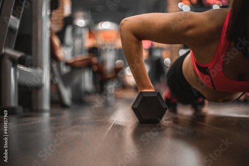 Fit woman young doing push ups exercise with dumbbells in the gym. © Inception