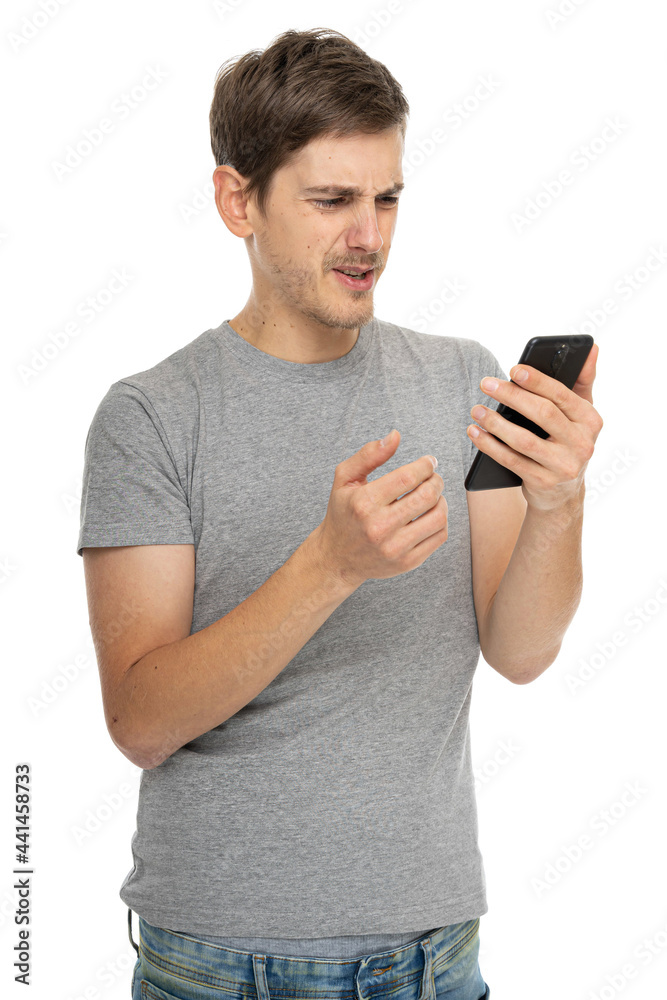 Young handsome tall slim white man with brown hair looks disappointed in gray shirt with mobile phone isolated on white background Young handsome tall slim white man with brown hair looks disappointed in gray shirt with mobile phone isolated on white background