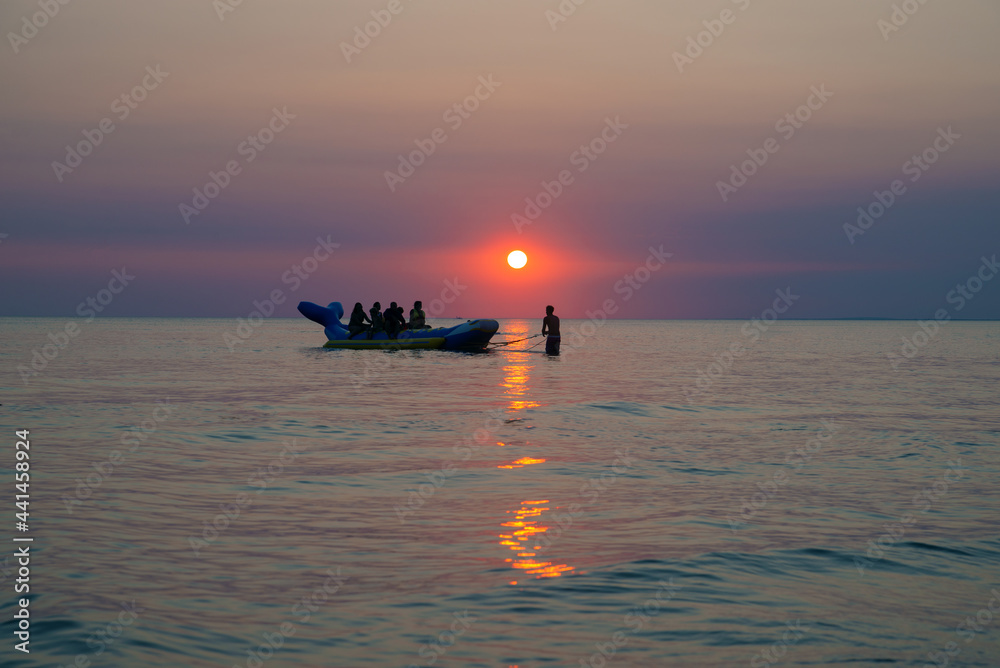 A group of tourists on an inflatable banana at sunset.. Inflatable banana shaped boat at sunset. Fun and good memories in the sea at sunset