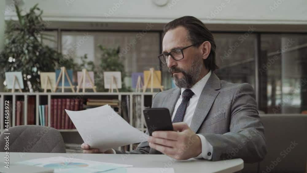Attractive businessman in business suit using smartphone in office texting on mobile phone uses a business app Attractive businessman in business suit using smartphone in office texting on mobile phone uses a business app