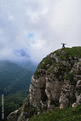 Traveler girl and her German Shepherd together on top of steep cliff against background of fog and sky before rain enjoy views and life. Tourist stands on mountain and spreads her arms out to sides.