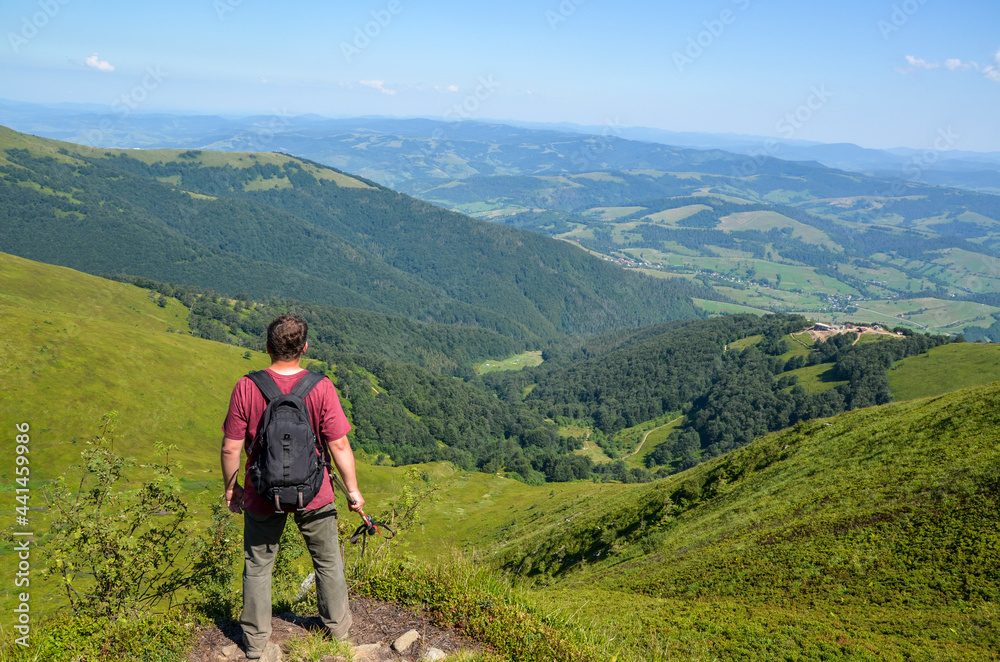 Back view of hiker with backpack and trekking sticks on top of mountain enjoying the view. Carpathian mountains, Ukraine