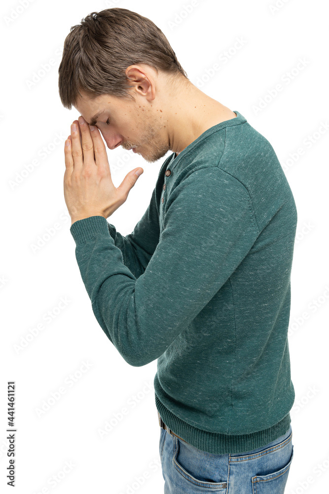Young handsome tall slim white man with brown hair praying staying sideways in dark green sweater in blue jeans isolated on white background Young handsome tall slim white man with brown hair praying staying sideways in dark green sweater in blue jeans isolated on white background