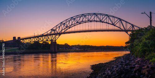 Sagamore Bridge Sunrise over Cape Cod Canal. Dawn Silhouette Architectural Image with Orange and Golden Colors. High Contrast Panoramic Seascape Image with Space for Text and Design. photo