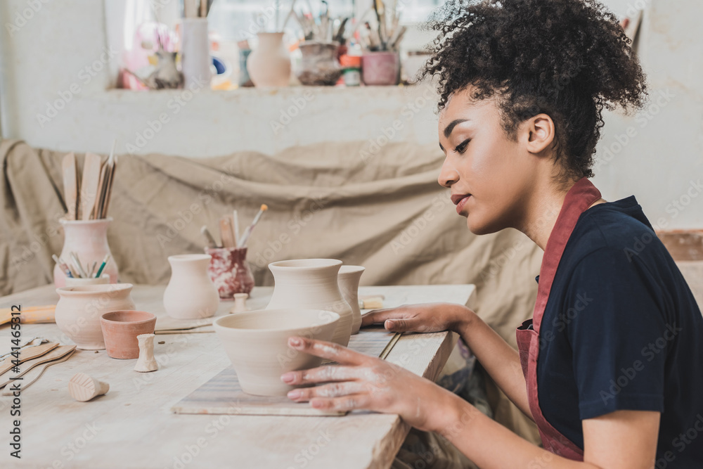 focused young african american woman sitting at table with clay pots in pottery focused young african american woman sitting at table with clay pots in pottery