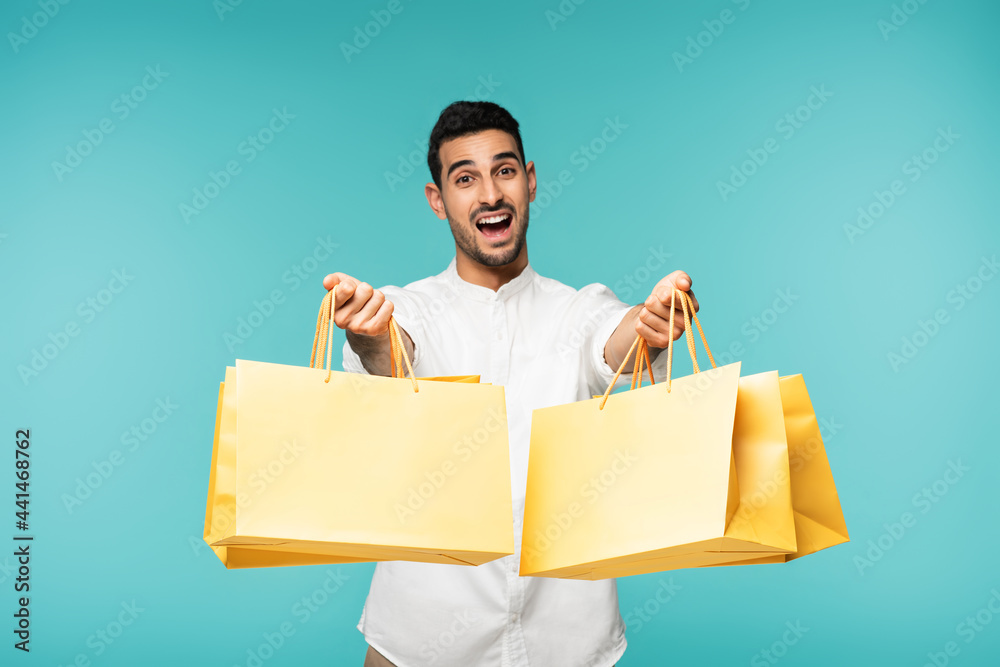 Excited arabian man holding shopping bags isolated on blue Excited arabian man holding shopping bags isolated on blue