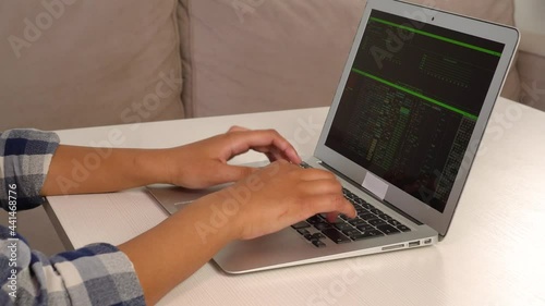 A young African-American woman quickly types text on a laptop keyboard while sitting at home. The concept of freelancing and working from home. The concept of a cybercriminal.