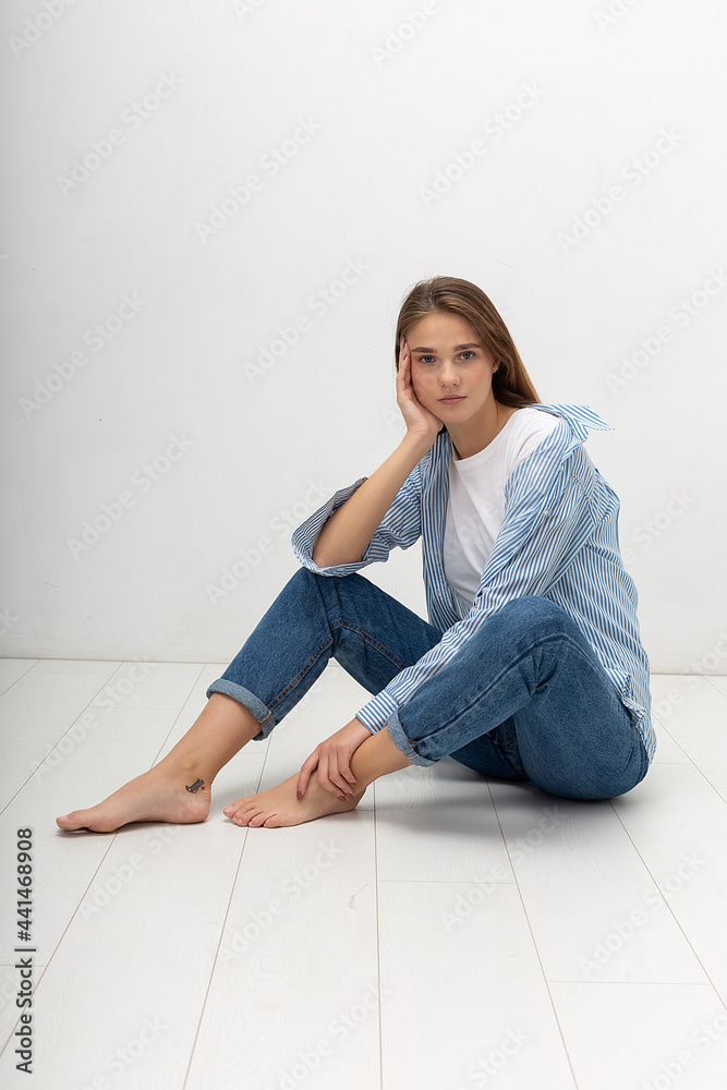 portrait of young attractive caucasian woman with long brown hair in t-shirt and blue jeans isolated on white background. skinny pretty female sitting on floor at studio. model tests of beautiful lady portrait of young attractive caucasian woman with long brown hair in t-shirt and blue jeans isolated on white background. skinny pretty female sitting on floor at studio. model tests of beautiful lady