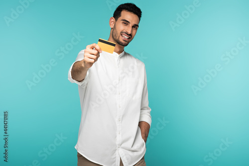 Credit card in hand of blurred arabian man smiling isolated on blue