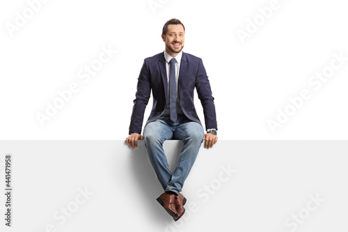Full length portrait of a man in jeans and suit sitting on a blank panel