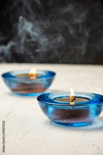 View of two burning candles in blue glass, on white table, with incense smoke, selective focus, black background, vertical, with copy space