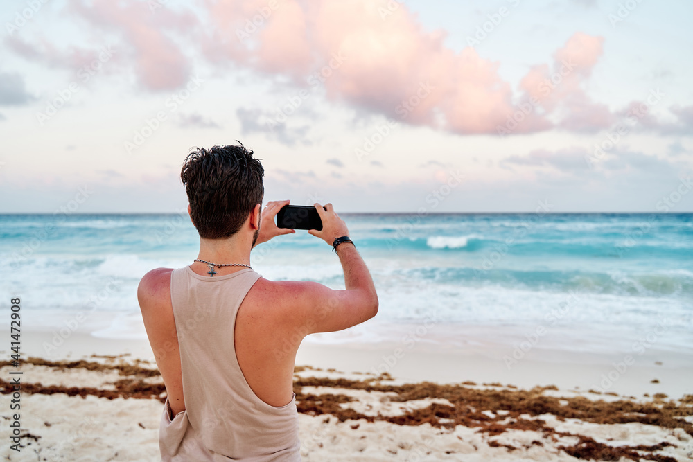 unrecognizable caucasian man with a cell phone in his hands taking pictures of the sunset at the sea of cancun