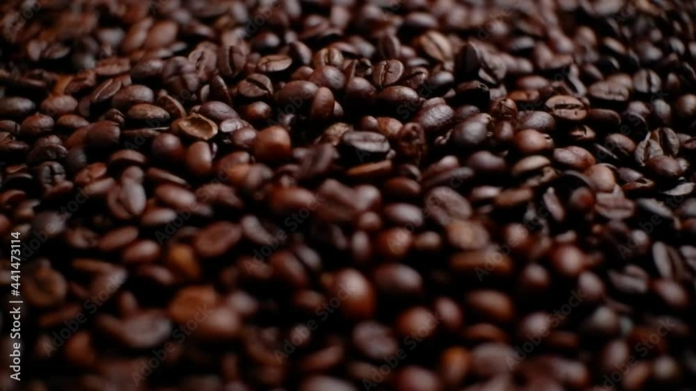 A small amount of coffee beans falling into a pile of coffee beans. Close-up. A small amount of coffee beans falling into a pile of coffee beans. Close-up.