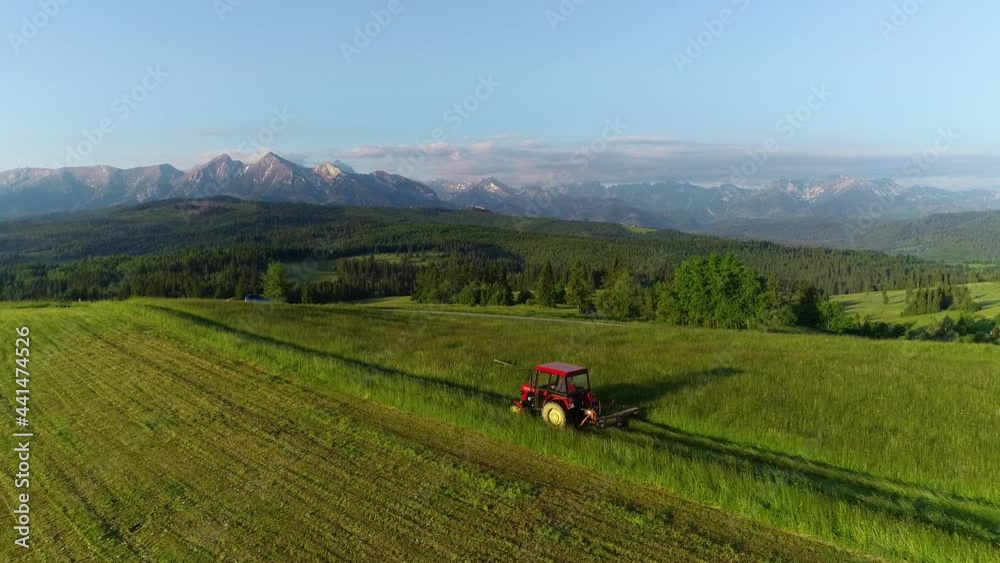 Aerial view of tractor mowing the grass. Alpine view and high mountains in the background. Haymaking in the mountain village. Agriculture machinery during harvest. Ecological agriculture. Aerial view of tractor mowing the grass. Alpine view and high mountains in the background. Haymaking in the mountain village. Agriculture machinery during harvest. Ecological agriculture.
