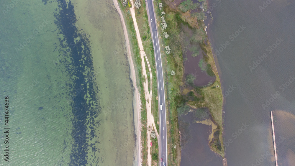 Fototapeta A highway that runs along a narrow spit between the sea and the estuary. Cars on the road. Aerial view.
