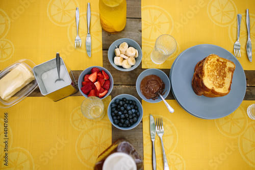 Preparing french toast with chocolate, banana, strawberry and blueberry on picnic table on a sunny morning photo