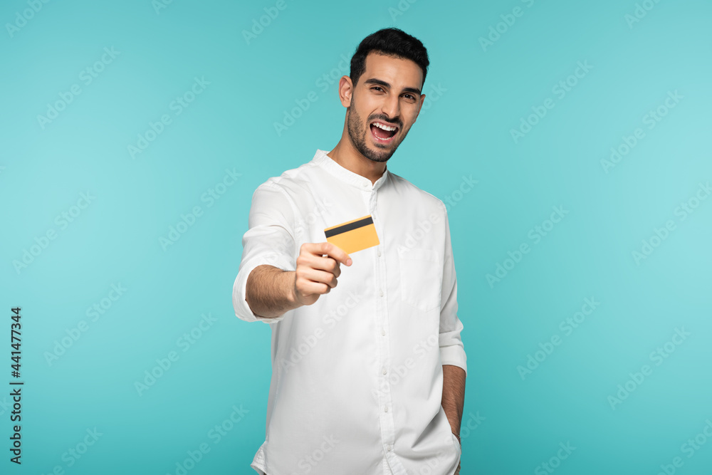 Cheerful arabian man showing credit card isolated on blue Cheerful arabian man showing credit card isolated on blue