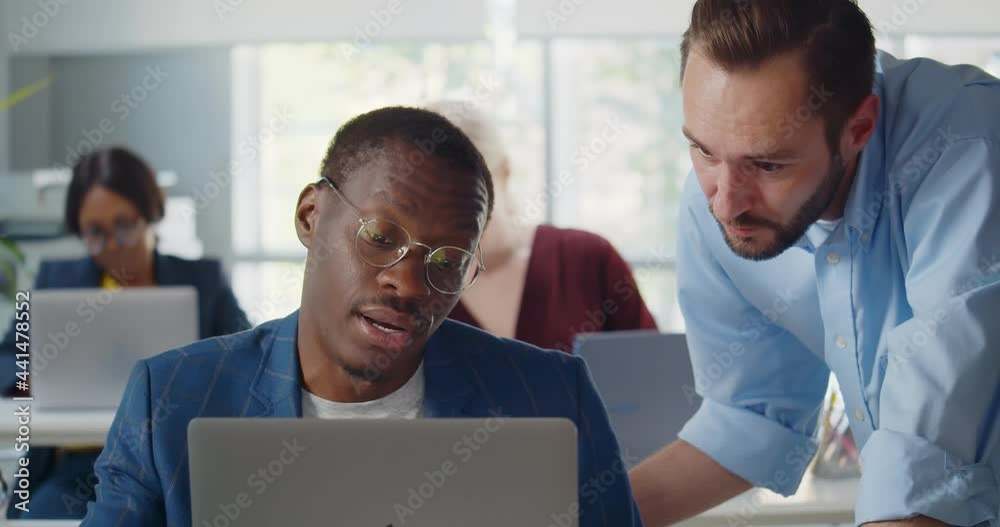 Young African businessman showing information on laptop to colleague Young African businessman showing information on laptop to colleague
