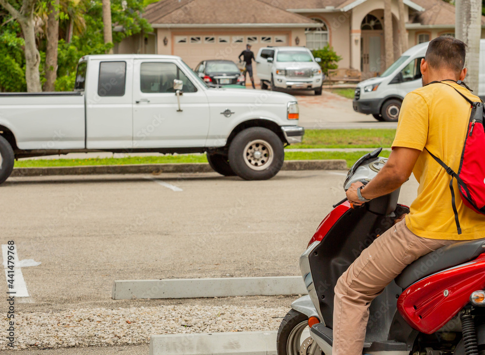 Man starting up a motor scooter with cars and a house in the background Man starting up a motor scooter with cars and a house in the background