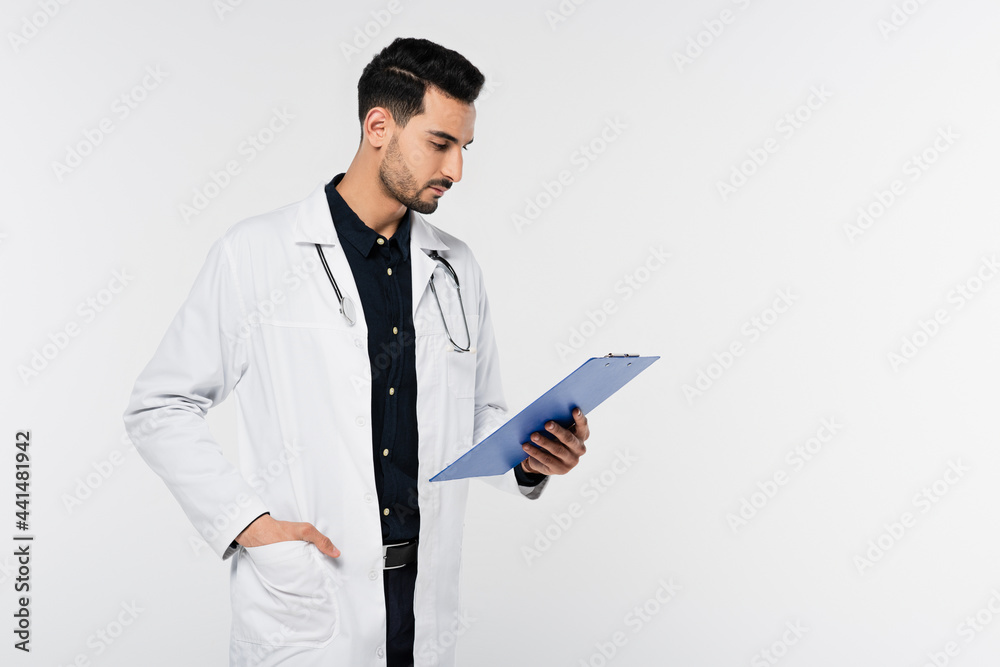 Arabian doctor looking at clipboard isolated on grey Arabian doctor looking at clipboard isolated on grey