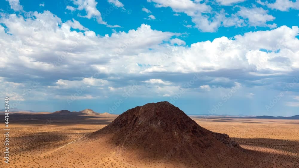 Huge cloud formations roll across the sky about the Mojave Desert towards volcanic cone-shaped mountains - time lapse