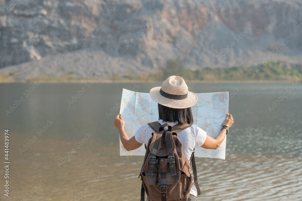 Asian woman enjoying beauty of nature looking at mountain lake Adventure travel. woman Traveler with map backpack relaxing outdoor with rocky mountains on background Summer vacations ,Lifestyle hiking