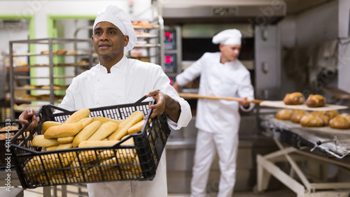 Portrait of male baker holding plastic crate with freshly baked bread in bakery