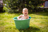 Baby girl flop in a green basin with water on home backyard in summer time